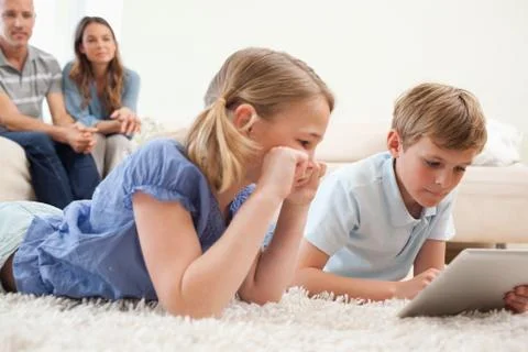 Children using a tablet computer with their parents on the background Stock Photos
