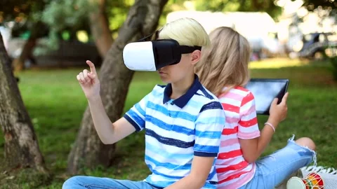 Children using VR glasses outdoor searching online on tablet in summer green Vidéo 138003268