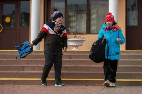 Children walk down steps after school in winter, carrying backpacks and weari Stock Photos