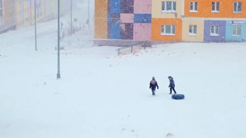 Children walk pulling big tire as snow tubing under snowfall 스톡 동영상 125994868