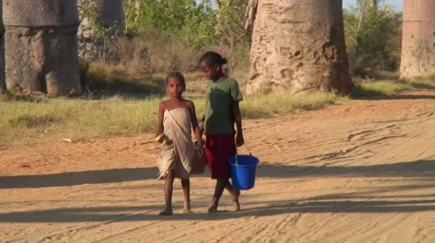 Children walking with plastic buckets in their hand on road in front of Baobabs Video stock 60608903