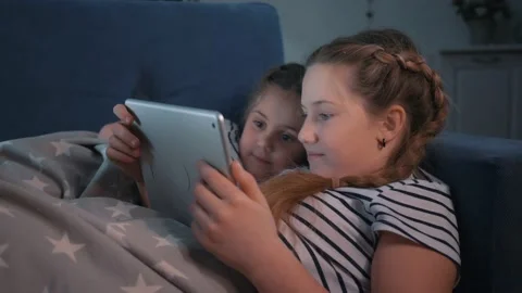 Children watch tablet lying on couch under warm blanket. Children watch movie on Video stock 233960453