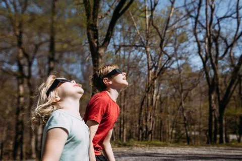 Children wearing solar eclipse glasses looking up at sun Foto stock