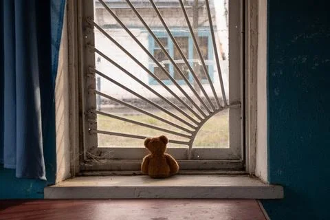 Children's brown bear sitting on a window with bars and looking out the windo Stock Photos