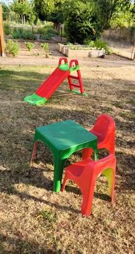 Childrens corner at the dacha: a bright table, chairs and a slide on green grass Stock Photos