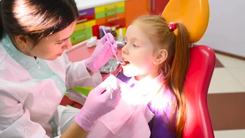 Children's dentist examines the teeth and mouth of a cute little red-haired girl Stock Footage 99995060