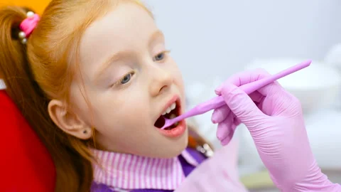 Children's dentist examines the teeth and mouth of a cute little red-haired girl Stock Footage 99995447