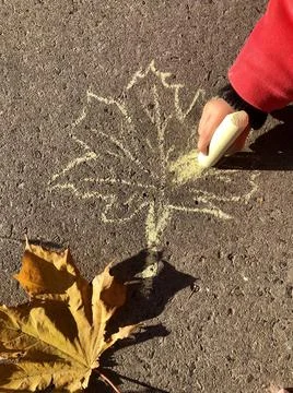 Children's hand draws maple leaf with yellow chalk on asphalt. The maple leaf Stock Photos