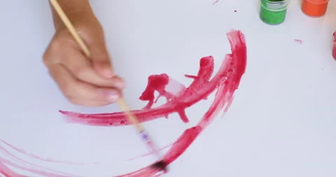Children's hand makes brush strokes with paint on white paper Stockbeeldmateriaal 223729633