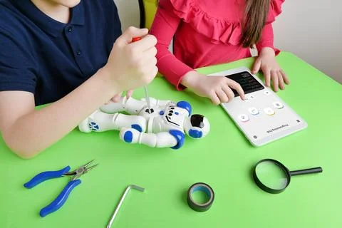 Children's hands assemble robot on workbench, screwing parts while reviewing Stock Photos
