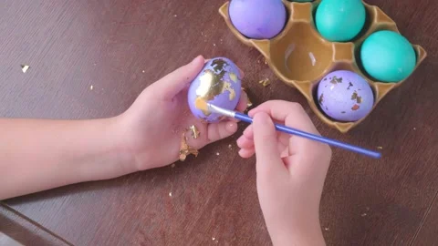 Children's hands decorate Easter eggs in gold leaf at wooden table at home. Stock Footage 164759820