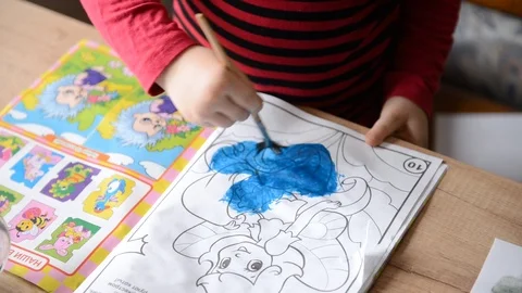 Children's hands draw coloring book watercolors on surface of wooden table on Stock Footage 104775780
