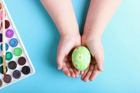 Children's hands hold a decorated Easter egg, on a blue background. Stock Photos