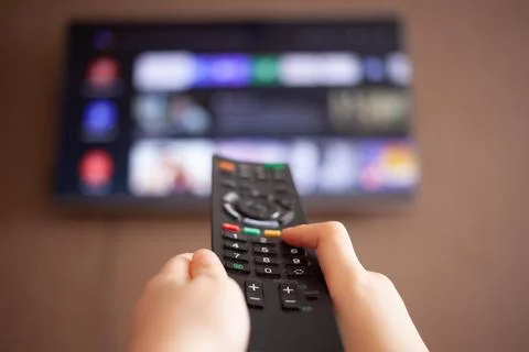 Children's hands hold a remote control on the background of a TV. Stock Photos