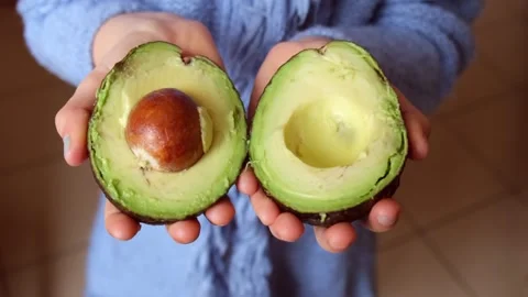 Children's hands holding an avocado cut in half Stock Footage 273672932