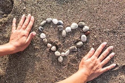 Children's hands making heart shape with stones on ground Stock Photos
