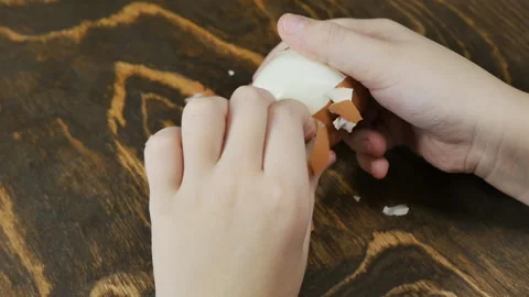 Children's hands peel a boiled egg from the shell on a wooden table top view Video stock 171875513