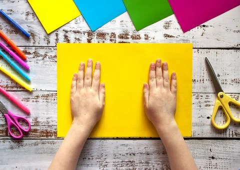 Children's hands, ready for creativity, lying on a sheet of yellow colored paper Stock Photos