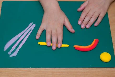 Children's hands sculpt a figurine of a rainbow and a sun from clay on the table Stock Photos