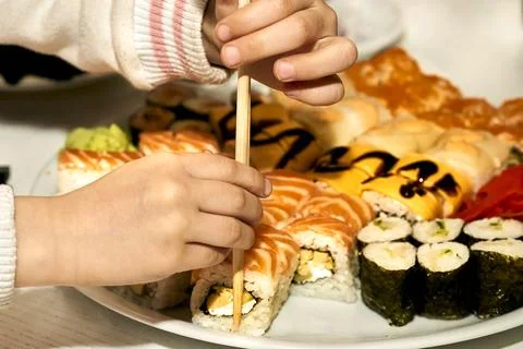 Children's hands taking delicious sushi with chopsticks. The child eats Stock Photos