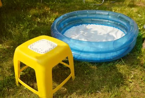 Children's inflatable pool and a small chair stand on the green grass on a Su Stock Photos
