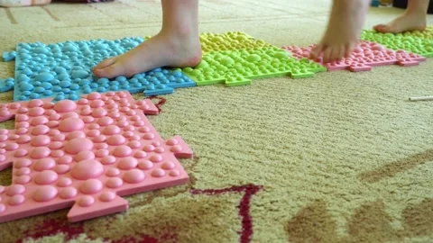 Children's legs go on a multi-colored massage orthopedic rug against a colored Stock Footage 160663933