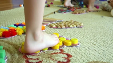 Children's legs go on a multi-colored massage orthopedic rug against a colored Stock Footage 160664008