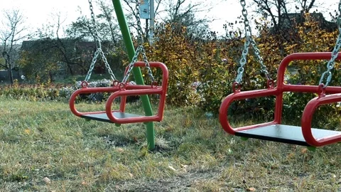 Children's playground in summer with the red swing, which is empty and swinging Stock Footage 106392003