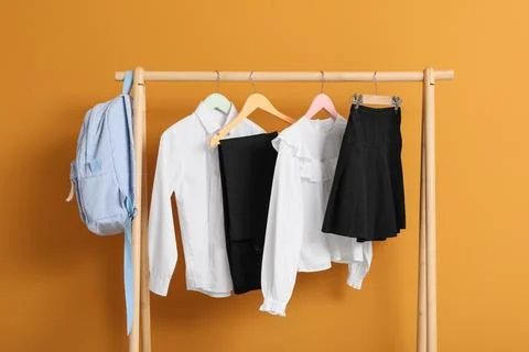 Childrens school uniform and backpack hanging on a wooden rack against a warm Stock Photos