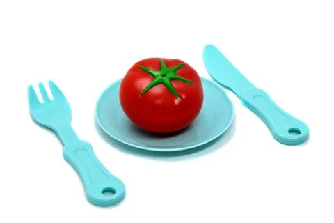 Children's toy plastic tableware: plate with tomato, fork and knife. Serving Stock Photos
