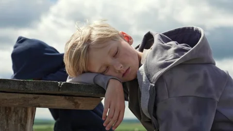 Child's Gentle Rest on a Weathered Bench Beneath a Soft Sky Stock Footage 338383764