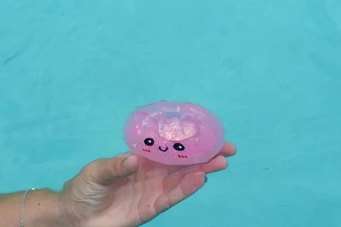 Child’s hand holding a dumpling squishy in clear blue pool water Foto stock