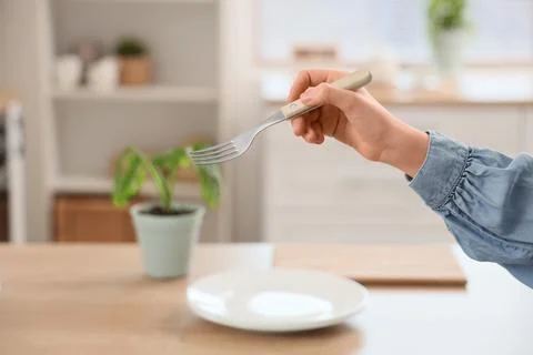 Childs hand holding a fork over an empty white plate on a wooden table in a b Stock Photos