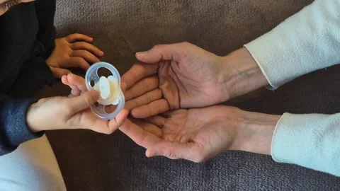 A child's hand holds a damaged pacifier while an adult assists 库存影片 301329862