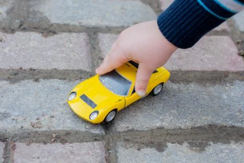 The child's hand leads a yellow toy car photo horizontal, close-up. Stock Photos