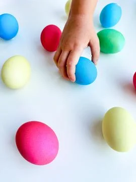 Child's hand picking up a blue Easter egg among colorful eggs on a white surface Foto stock