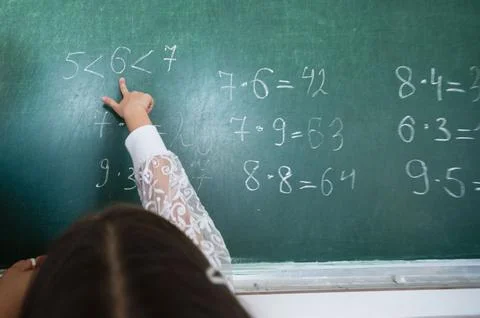 A child's hand points to a chalkboard with math problems, highlighting educat Stock Photos