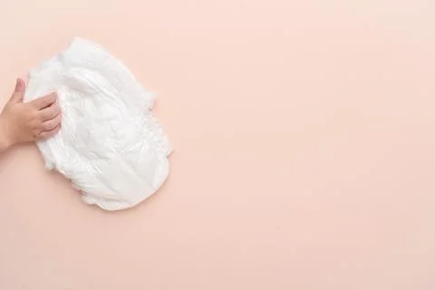 A child's hand is pulling a diaper-panties on a beige background. Stock Photos