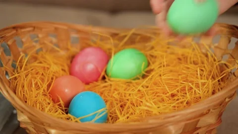A child's hand puts Easter colored eggs in a yellow wicker basket. Holiday Stock Footage 169823029