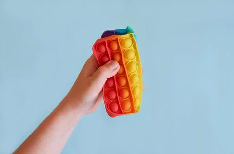 A child's hand squeezed in half a square silicone toy Pop It. Stock Photos