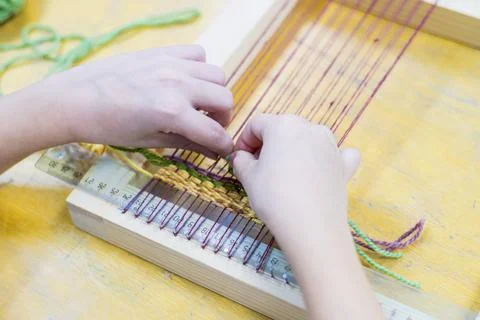 The child's hands are weaving a pattern of multi-colored threads on a weaving Foto stock