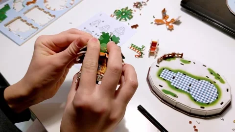A child's hands attach a tree-shaped roof to a miniature house in this step.. Stockbeeldmateriaal 316595312