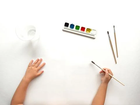Childs hands begin creative art project with paints and brushes Stock Photos
