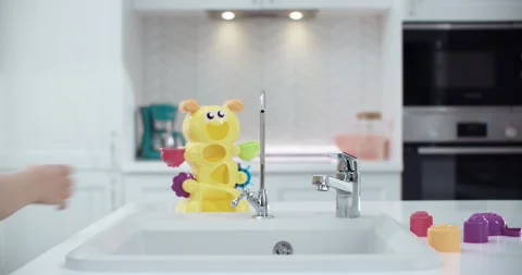 Child’s hands in the kitchen draw filtered water in a yellow toy. Vidéo 230644555