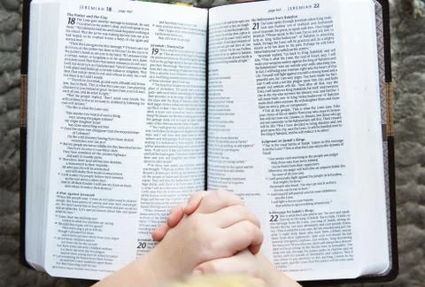 Child's Hands Praying Over Open Holy Bible Stock Photos