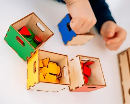 A childs hands sort flat geometric shapes by color into four boxes: red, yellow Stockfoto's