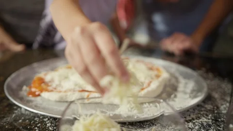 Child's hands sprinkling shredded cheese on pizza in kitchen Stock Footage 123733220
