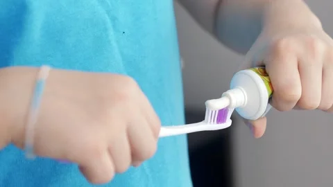 A child's hands squeeze toothpaste onto a toothbrush from a tube in the bathroom Stock Footage 261988659