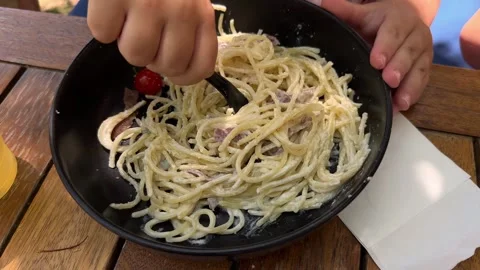 Child's hands try to use fork taking spagetthi carbonara into his plate Stock Footage 287804407