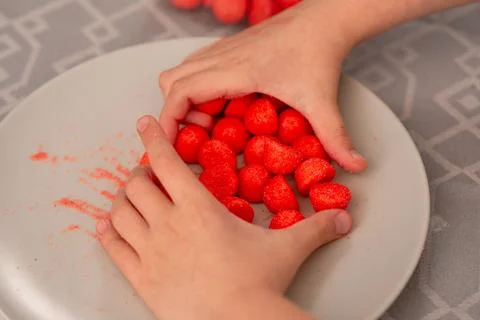 Child's playtime delight tiny hands reaching for red fruity candies on a pl.. Stock Photos